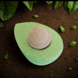Green bath bomb with a pink center on a dark surface with green leaves.
