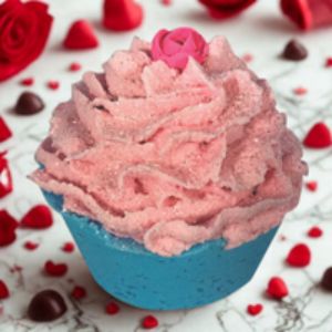 Pink bath bomb with a blue base on a white surface with red roses and chocolate pieces.