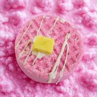 Pink bath bomb with a yellow center and white drizzle on a pink fluffy background