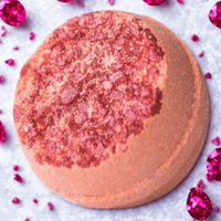 Round pink bath bomb with a textured surface on a white background with red flowers.